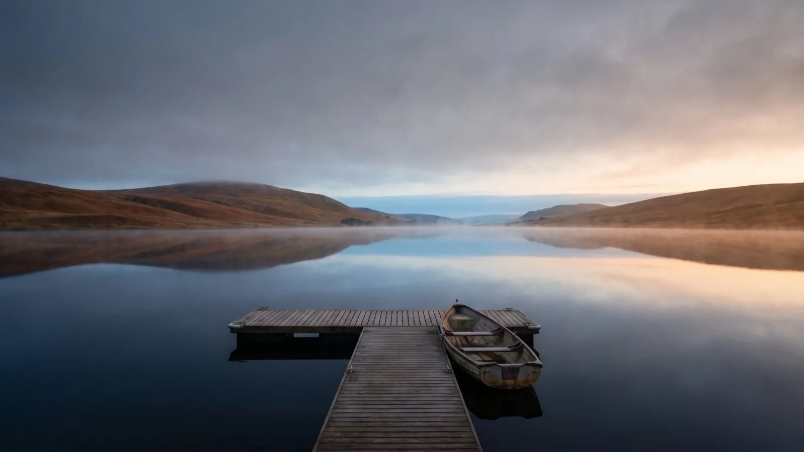 A calm lake at dawn reflecting rolling hills
